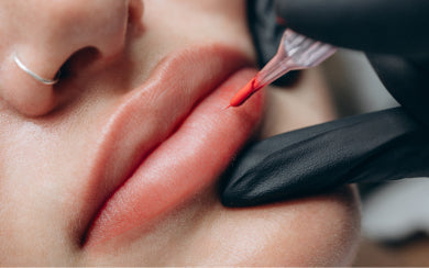 Gloved PMU artist applying pigment to a client’s lower lip.