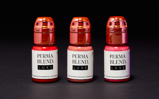 Three bottles of Perma Blend Luxe permanent makeup pigments in red, nude, and pink shades lined up against a black background.